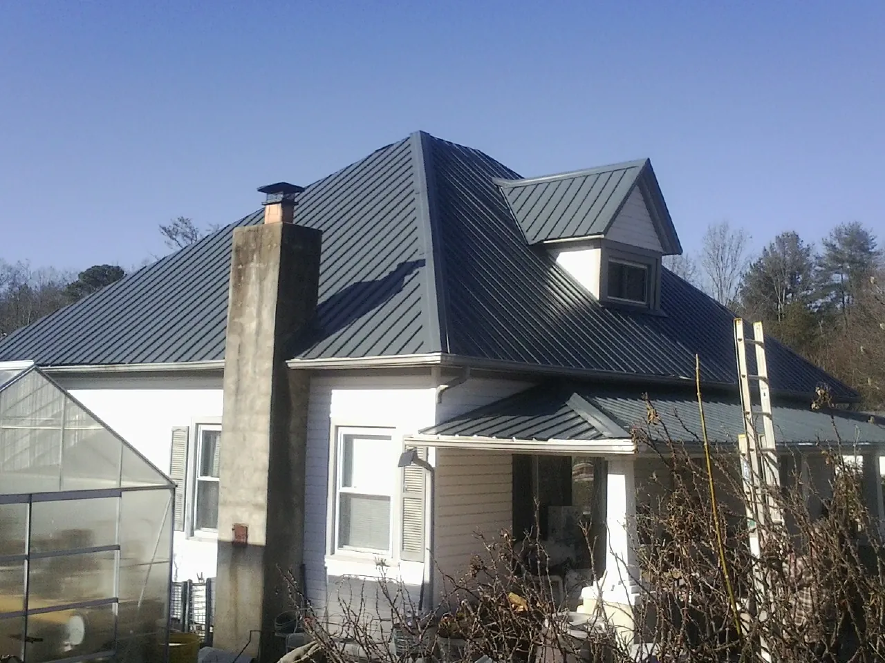 Dark blue standing seam metal roof on a white farmhouse with dormer — Slate & Tile Roof Repair by Roofing Brothers in Cypress Inn
