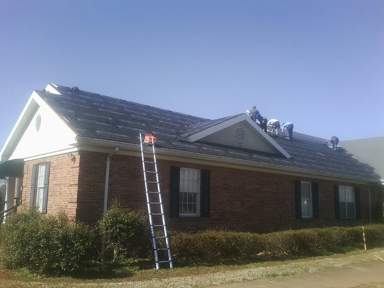 Crew tearing shingles off a brick ranch roof with a ladder set — Metal Roof Repair work by our crew in Cypress Inn