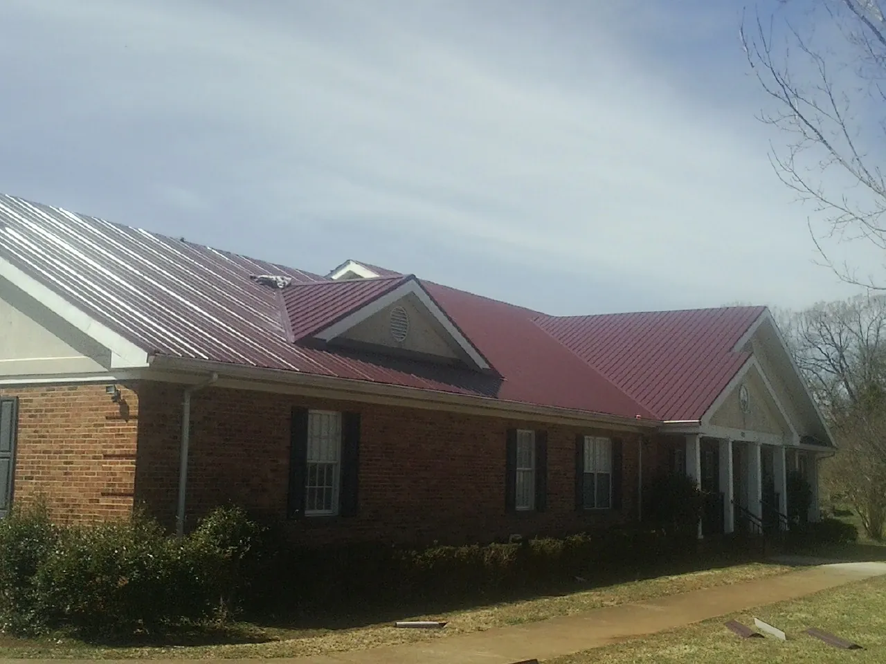 Red metal roof with gabled entries on a long brick building, from a Hail Damage Roof Repair job in Cypress Inn
