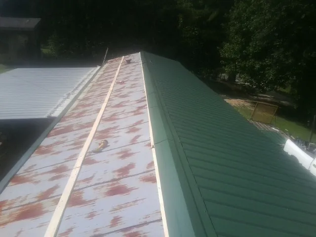Old rusted panels beside newly installed green metal roofing — Wind Damage Roof Repair by Roofing Brothers in Cypress Inn