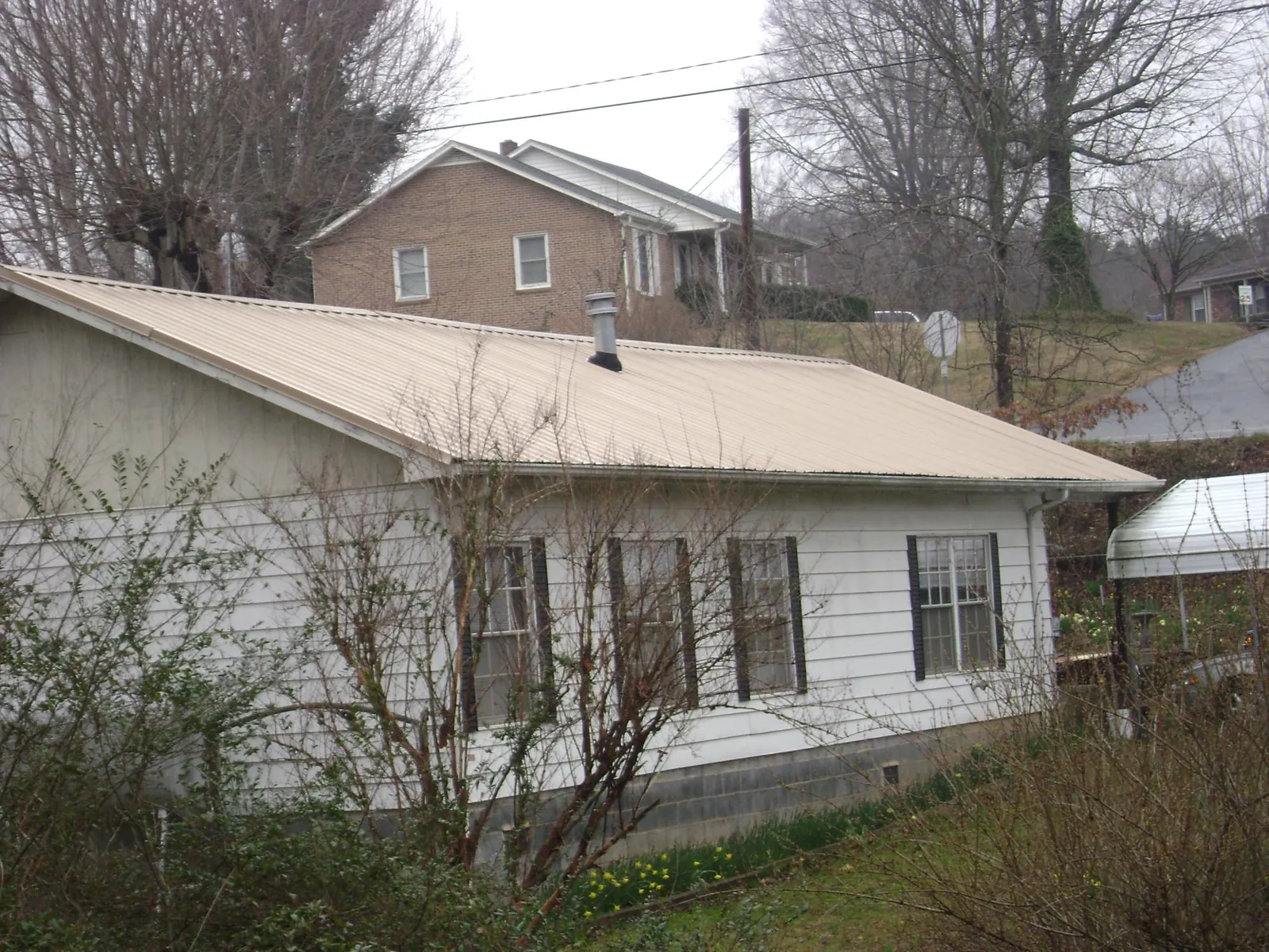Tan metal roof on a white sided house set into a hillside — Commercial Roofing by Roofing Brothers in Cypress Inn