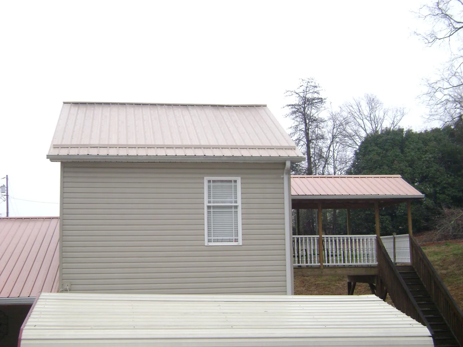 Tan metal roofs on a two story addition and attached porch, from a Roof Replacement job in Cypress Inn
