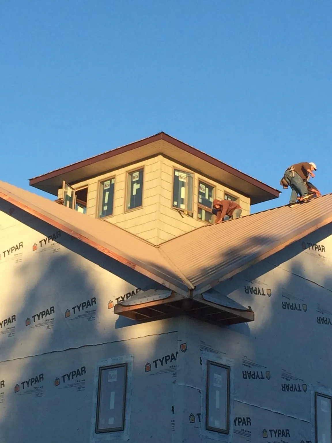Roofers working around a rooftop cupola on a new metal roof at sunset — Roof Waterproofing in Cypress Inn by Roofing Brothers